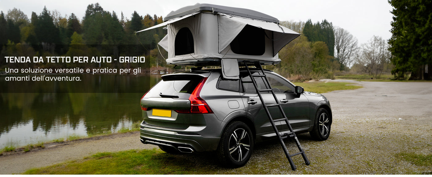 Tenda da tetto grigia montata su SUV verde, con scala, immersa in un paesaggio naturale vicino a un lago tranquillo