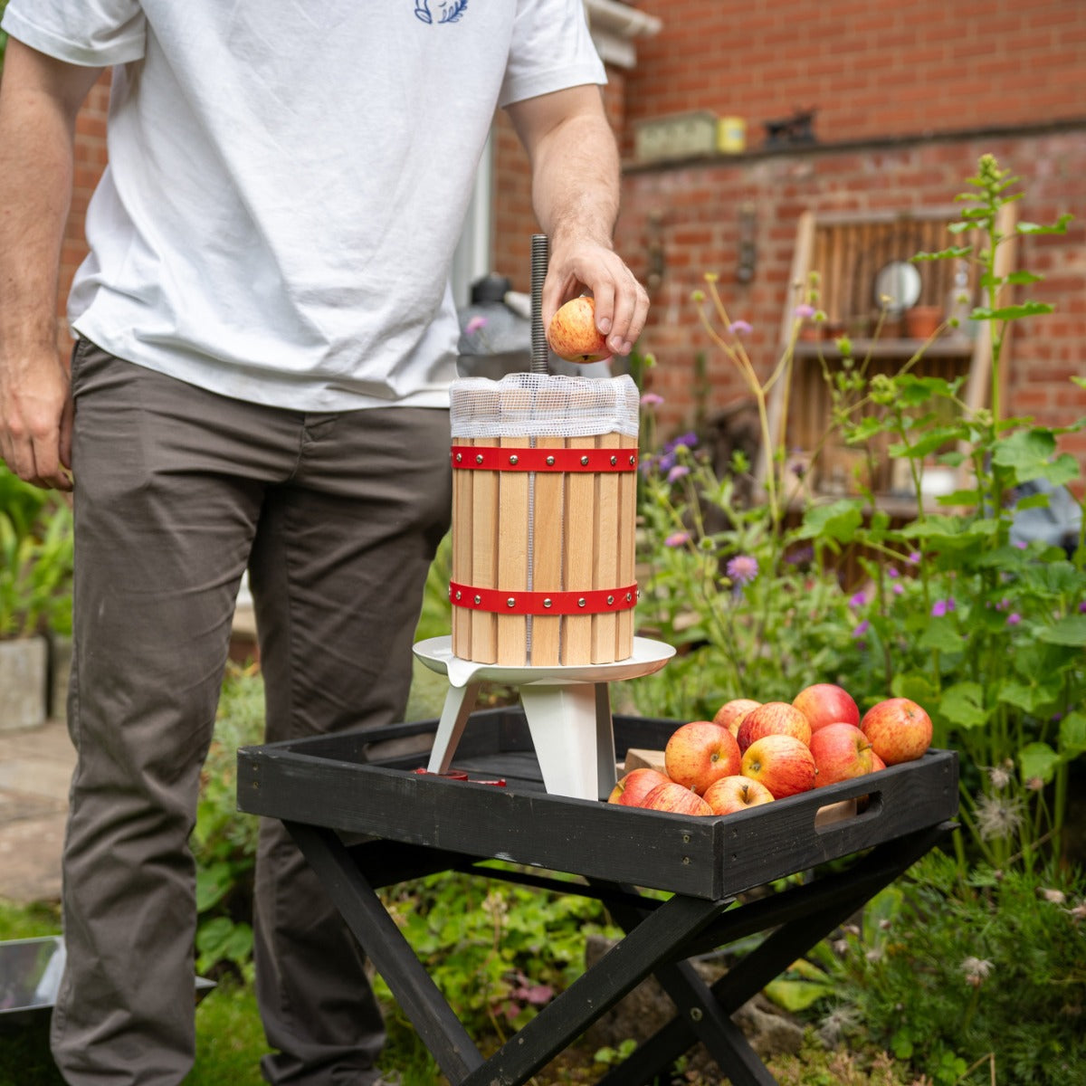 Torchio per frutta in legno con dettagli rossi, utilizzato per spremere mele fresche in un giardino, circondato da frutta raccolta