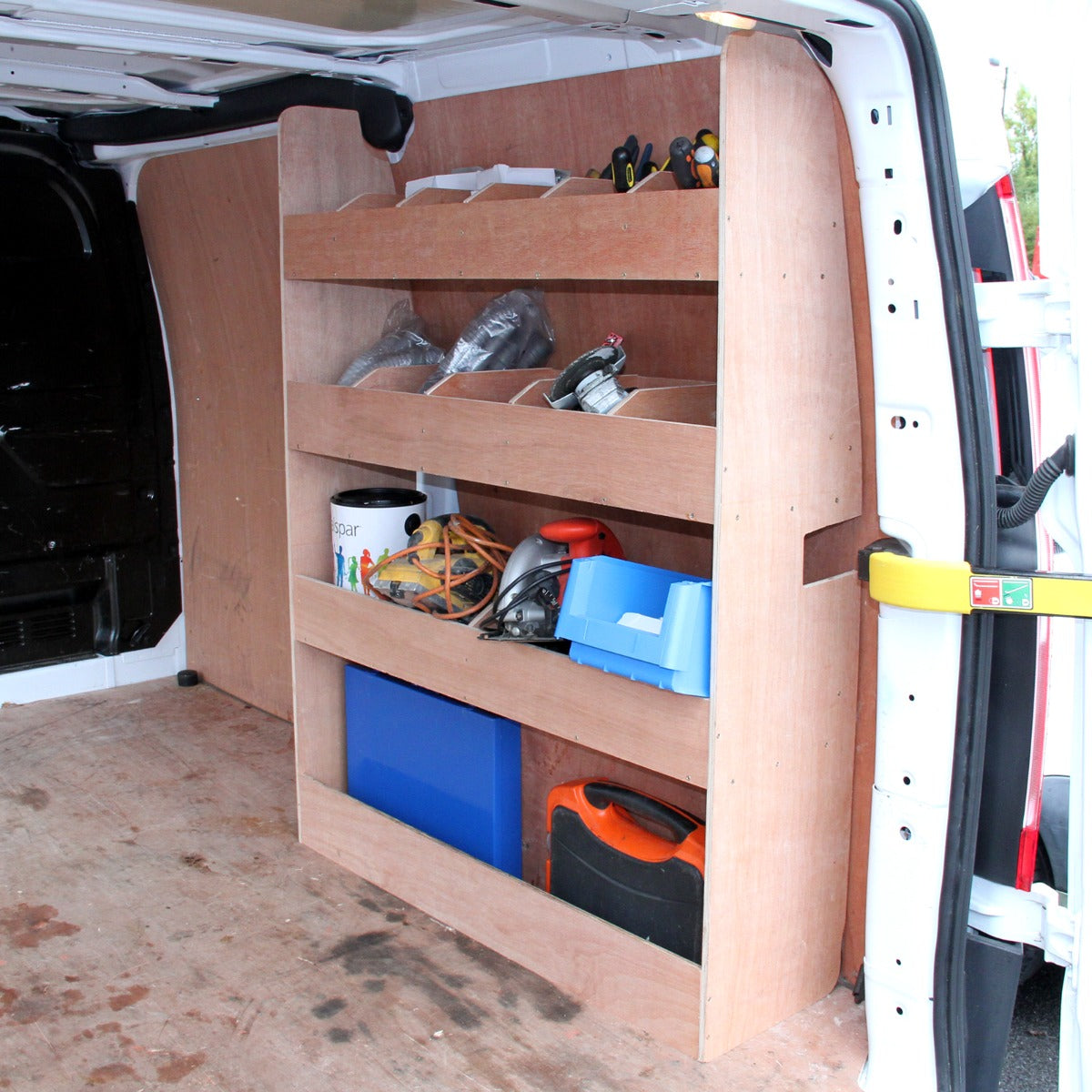 Scaffale in legno chiaro per furgone Ford Transit, con tre ripiani e attrezzi vari, su sfondo di tappezzeria grigio fumo