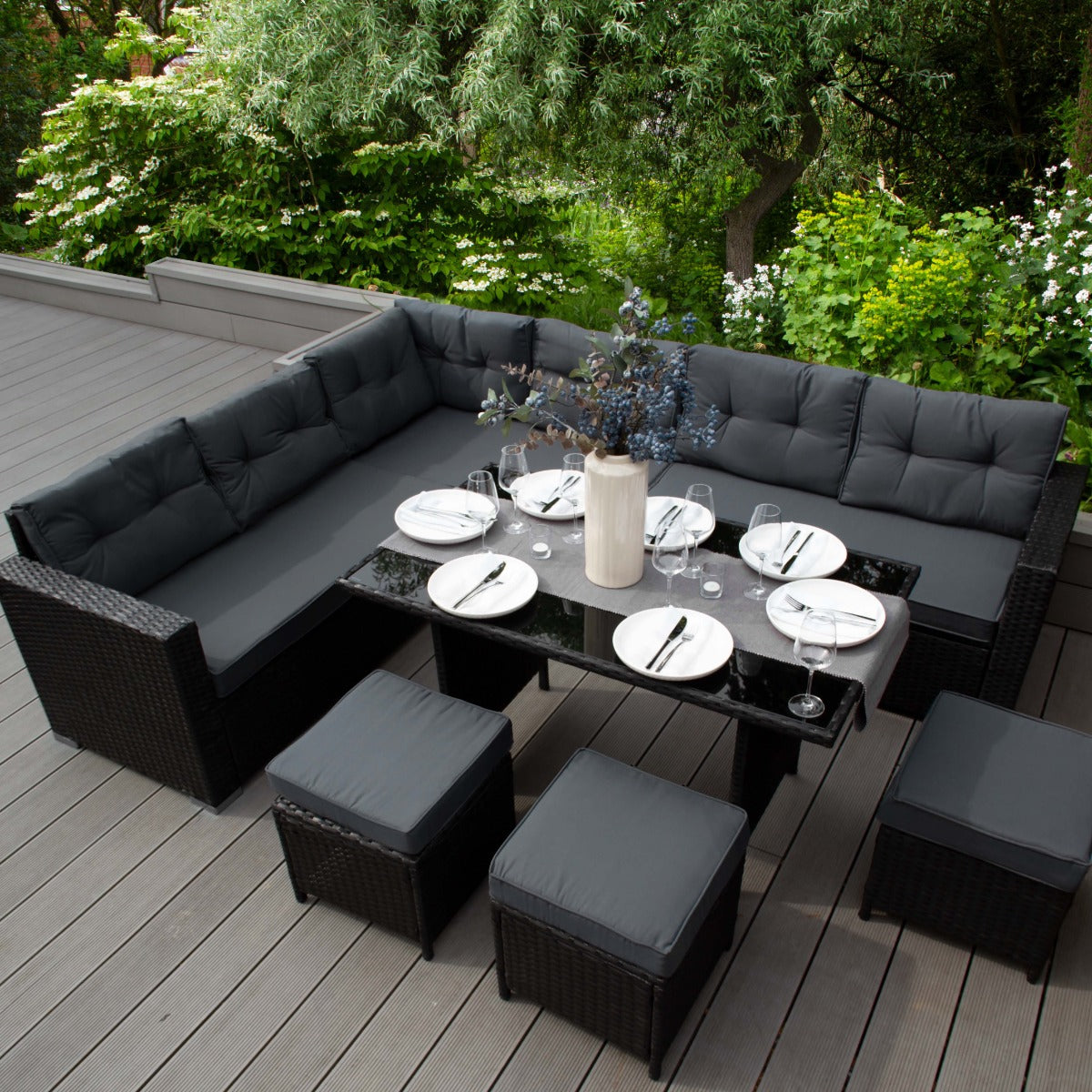 Set ad angolo in rattan nero con cuscini grigi, tavolo in vetro, decorato con fiori, ideale per esterni eleganti e confortevoli