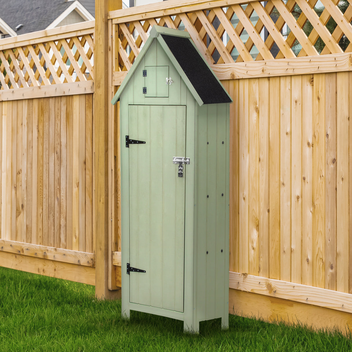 Casetta da giardino in legno verde con tetto nero, porte in legno e serratura, posizionata su un prato verde vicino a una recinzione di legno