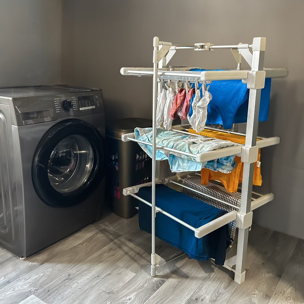 Stendibiancheria elettrico riscaldato in plastica bianca, con ripiani per asciugare vestiti colorati in un ambiente domestico moderno