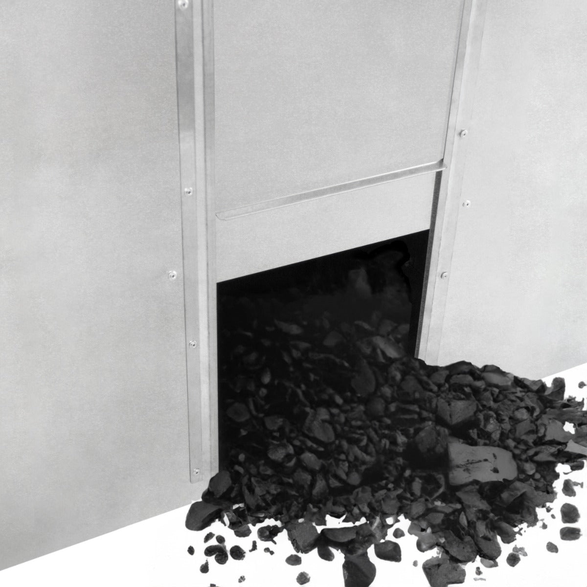 Bidone per carbone e legna in metallo grigio con apertura, carbone nero sparso sul pavimento, design robusto e funzionale