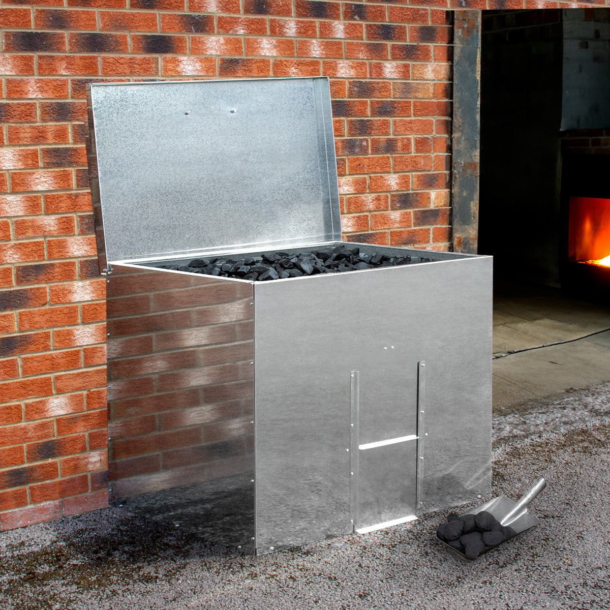 Bidone per carbone e legna in acciaio inox, con coperchio aperto, riempito di carbone, posizionato accanto a un muro di mattoni rossi