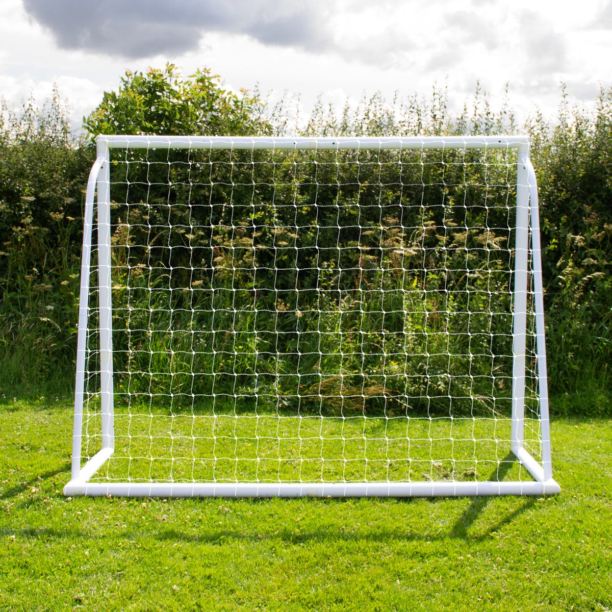 Porta da calcio bianca di 240cm x 180cm con rete trasparente, posizionata su un prato verde, circondata da vegetazione naturale
