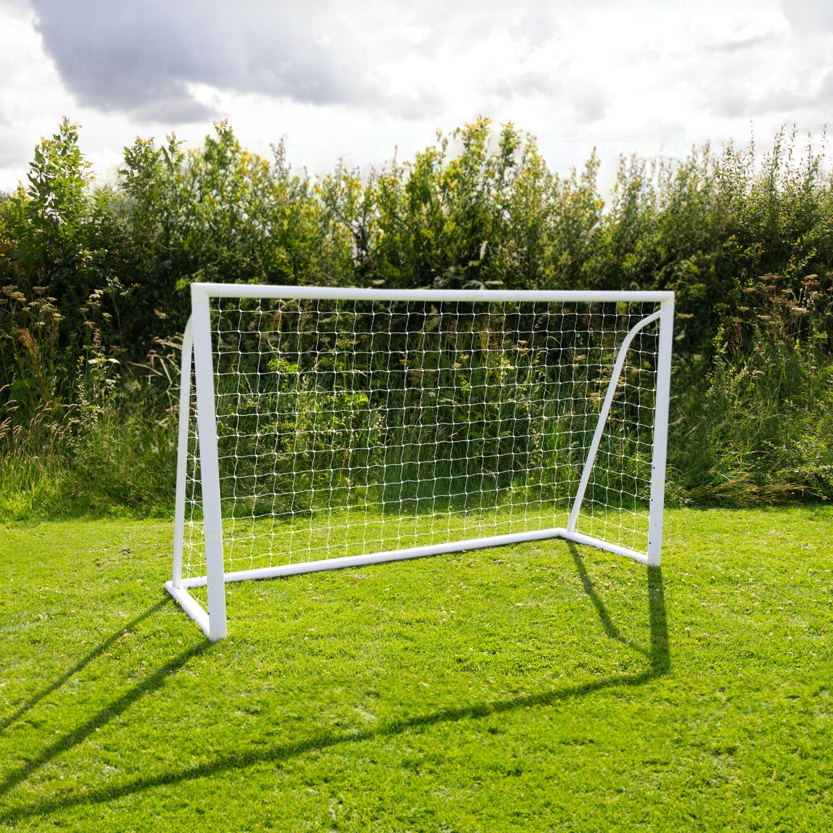 Porta da calcio bianca da 180cm x 120cm con rete, posizionata su un campo verde, circondata da alberi e cielo nuvoloso