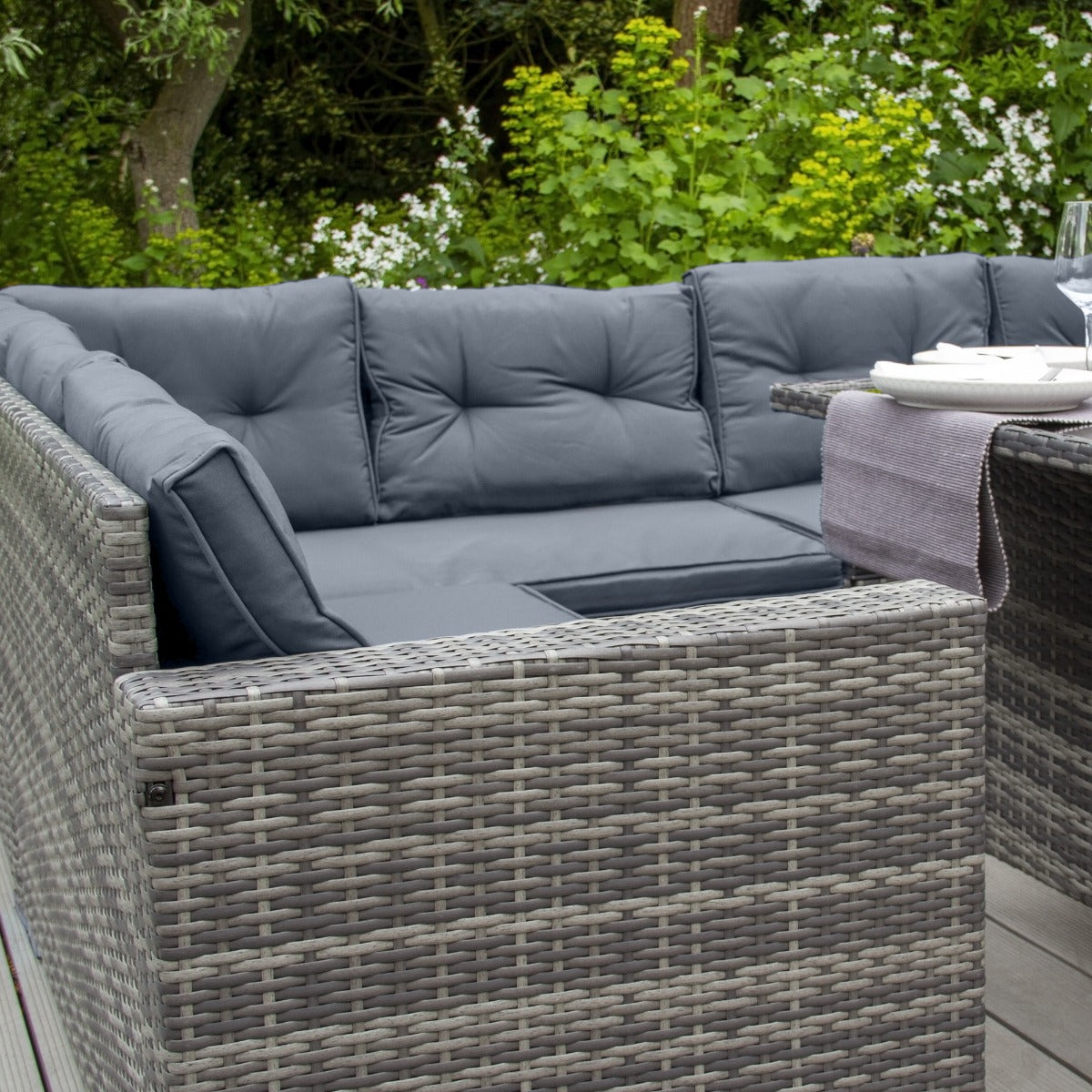 Set ad angolo in rattan grigio con cuscini blu scuro, ideale per esterni, con texture intrecciata e design moderno