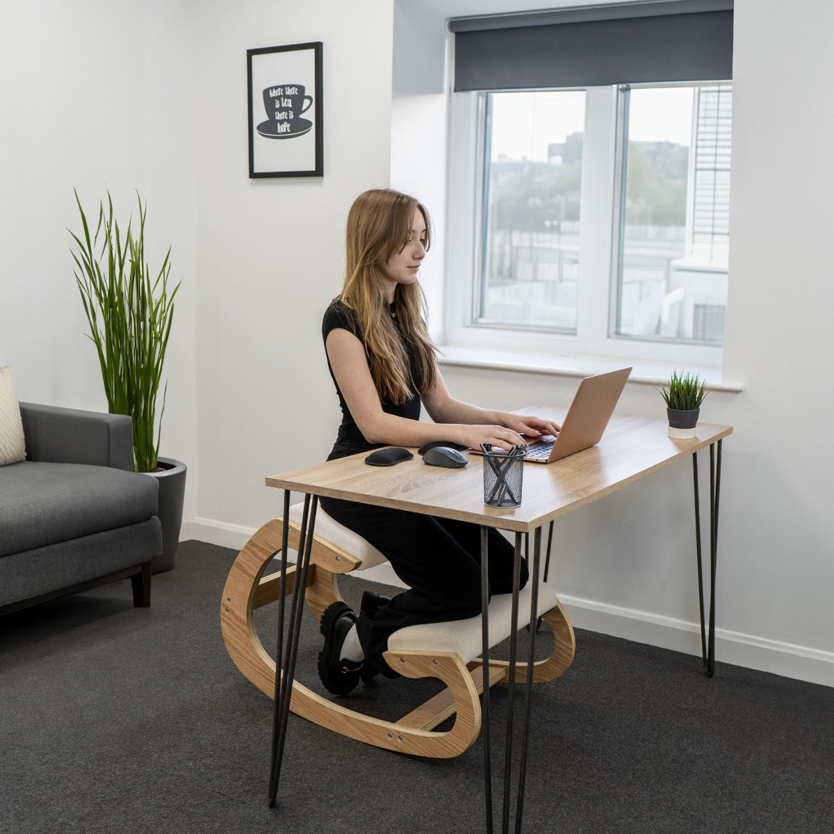 Sedia ergonomica da inginocchiarsi in legno chiaro, con superficie liscia e design curvo, utilizzata da una donna al computer in un ambiente moderno