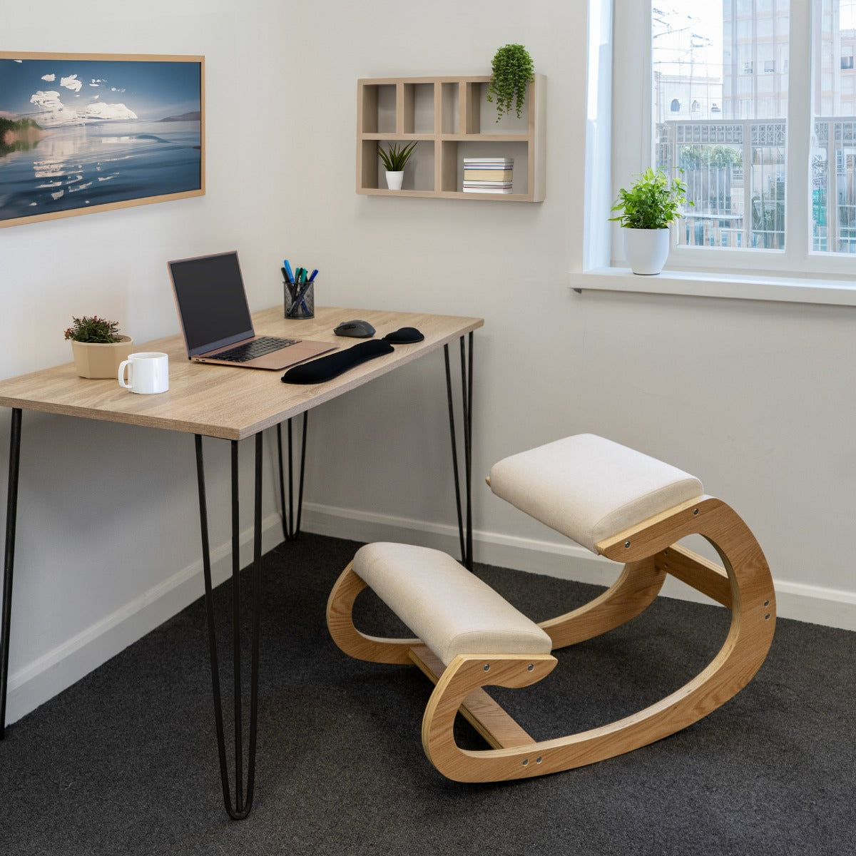Sedia ergonomica da inginocchiarsi in legno chiaro con cuscini beige, posizionata accanto a un tavolo moderno in un ufficio luminoso