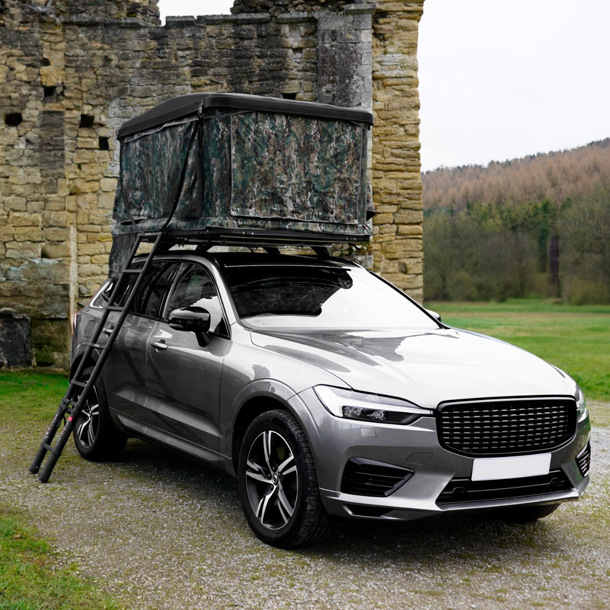 Tenda da tetto mimetica montata su un'auto grigia, con struttura robusta e tessuto resistente, in un paesaggio naturale verde