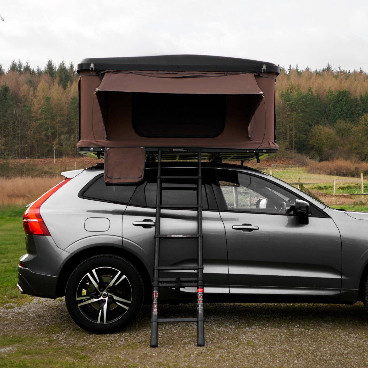 Tenda da tetto marrone montata su un'auto grigia, con scala in metallo, ideale per campeggio e avventure all'aperto