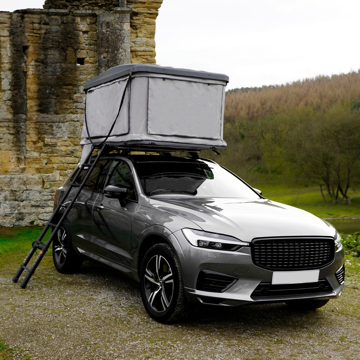 Tenda da tetto grigia montata su un'auto grigia, con struttura robusta e aste di supporto, immersa in un paesaggio naturale verde