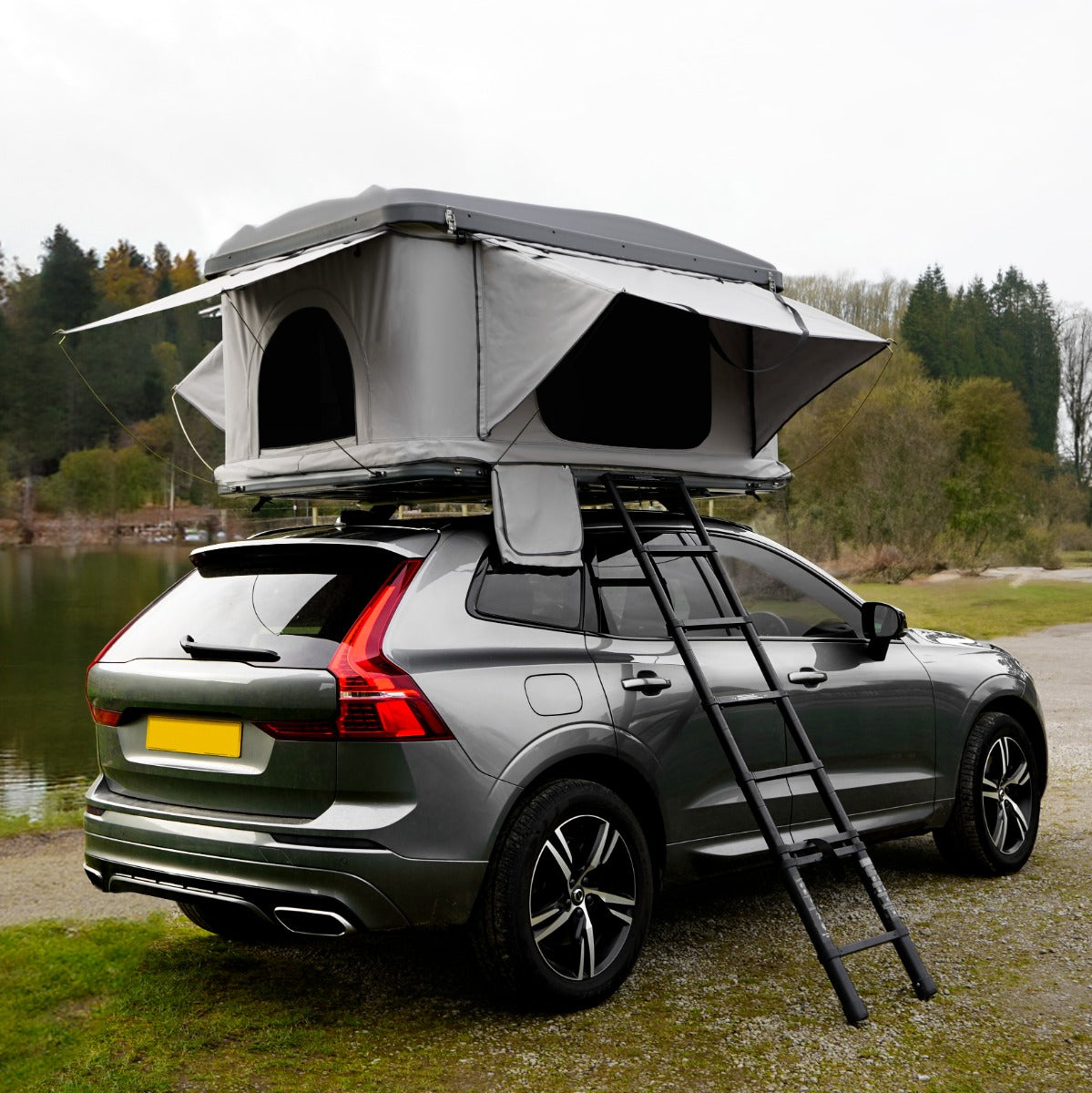 Tenda da tetto grigia montata su un'auto grigia, con aperture laterali e scala per l'accesso, immersa in un paesaggio naturale