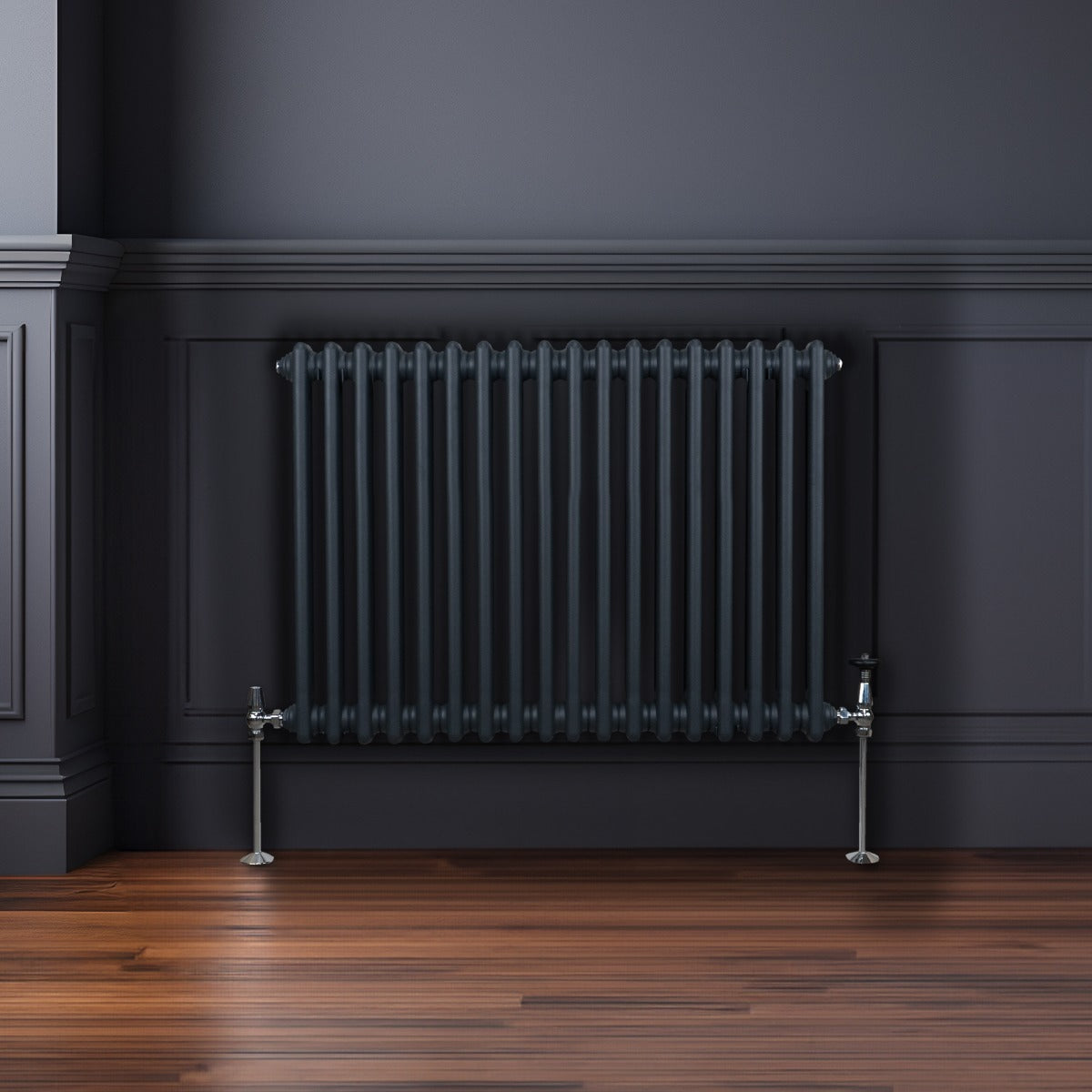 Termosifone a 2 colonne grigio antracite, con finitura liscia e tubi verticali, montato su parete scura e pavimento in legno lucido