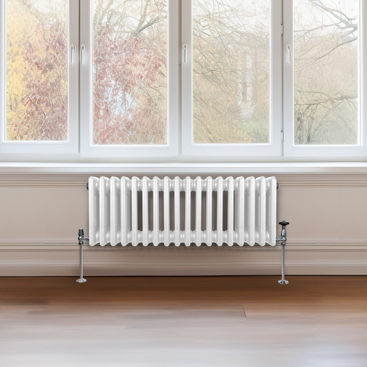 Termosifone a 3 colonne bianco, con finitura liscia e lucida, posizionato sotto una finestra con vista su alberi autunnali