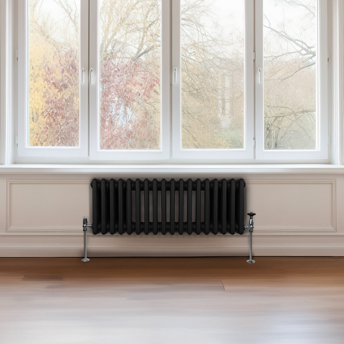 Termosifone a 3 colonne di colore nero, elegante e moderno, posizionato sotto una finestra con vista su un paesaggio autunnale
