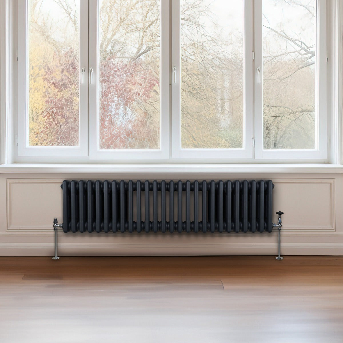 Termosifone a 3 colonne grigio antracite, elegante e moderno, installato sotto una finestra con vista su un paesaggio autunnale