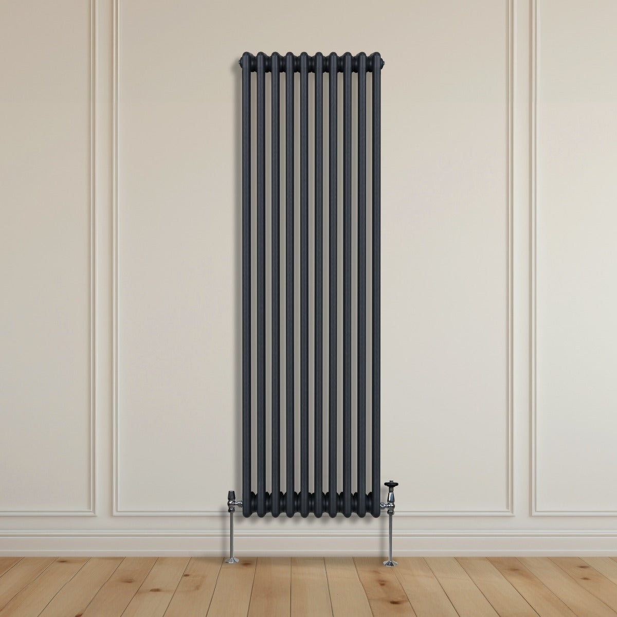 Termosifone a 3 colonne grigio antracite, alto e stretto, con finitura liscia e tubi verticali, installato su parete chiara con pavimento in legno