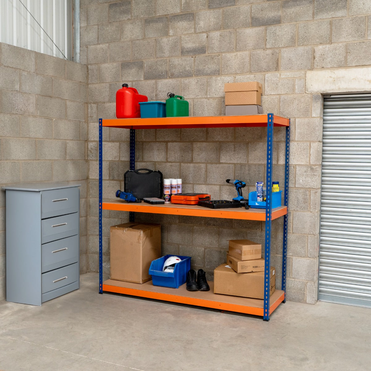Scaffalatura a 3 ripiani in metallo blu e arancione, con scatole, attrezzi e contenitori, posizionata in un garage con pareti grigie