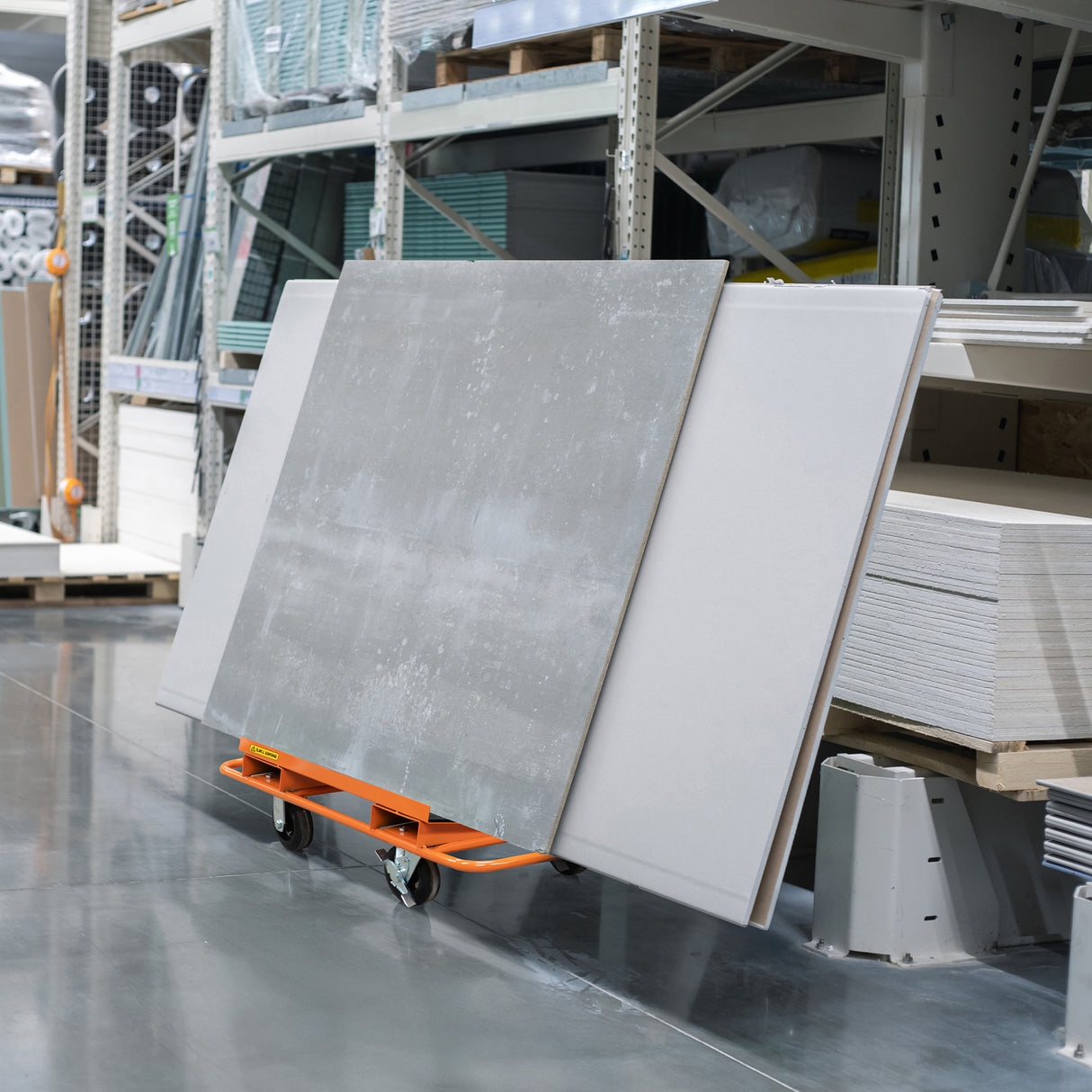Carrello arancione per cartongesso, carico di pannelli grigi, con ruote robuste, posizionato in un magazzino ben organizzato