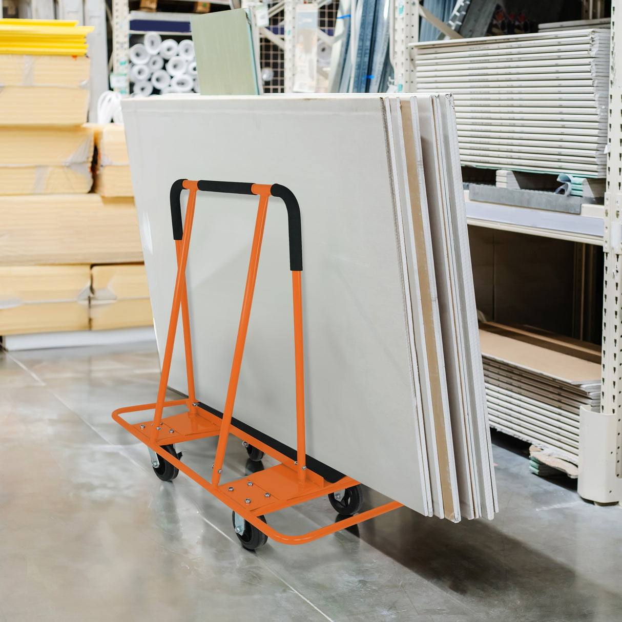 Carrello arancione per cartongesso, progettato per trasportare lastre fino a 1000 kg, con ruote e manico ergonomico in un ambiente di magazzino