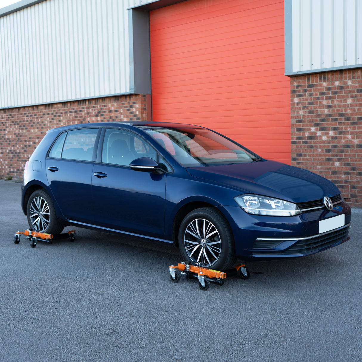 Pattini di posizionamento idraulici arancioni sotto una Volkswagen Golf blu, su una superficie grigia, per facilitare il sollevamento dell'auto