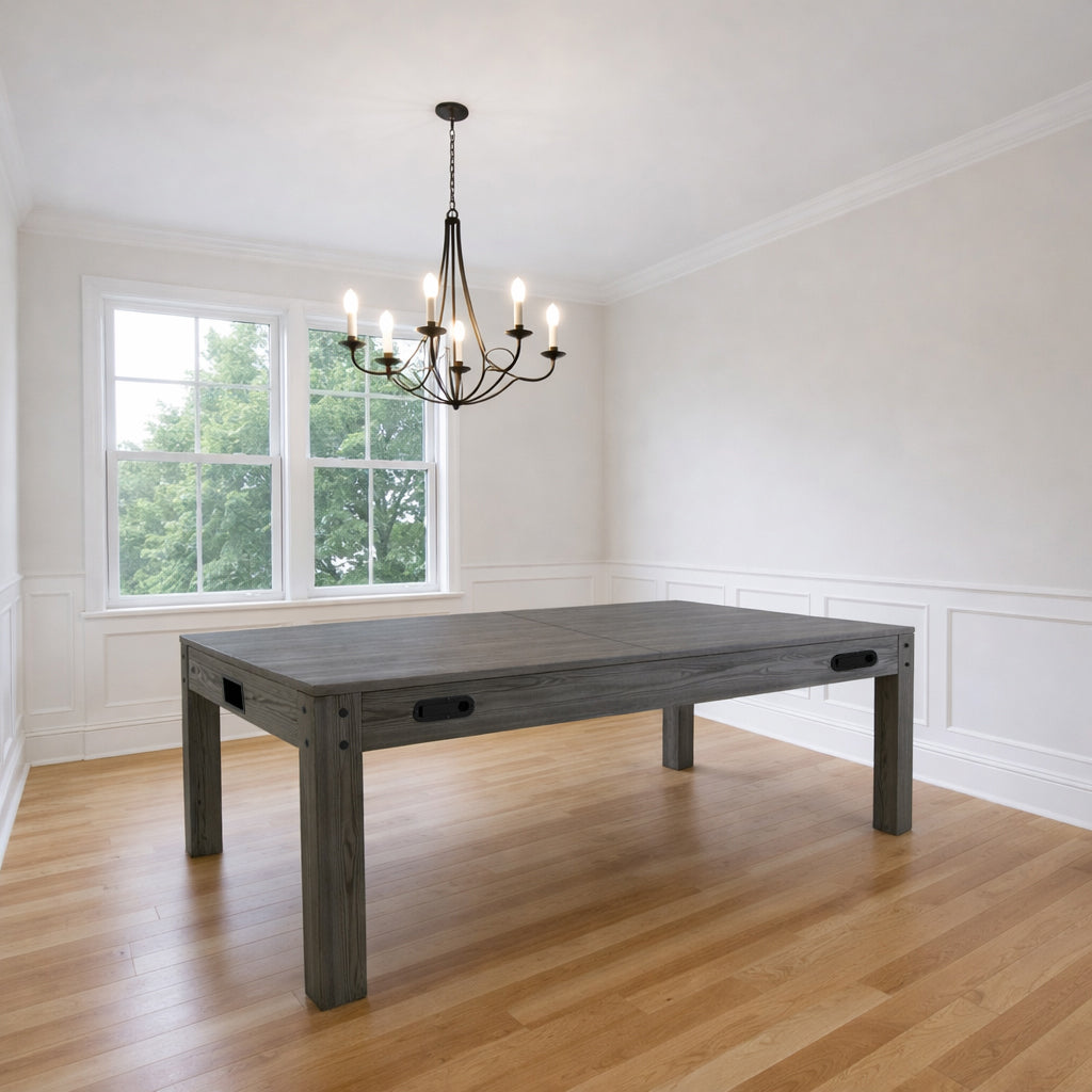 Tavolo multigioco 7-in-1 in legno grigio, superficie liscia e robusta, posizionato in una stanza luminosa con pavimento in legno chiaro