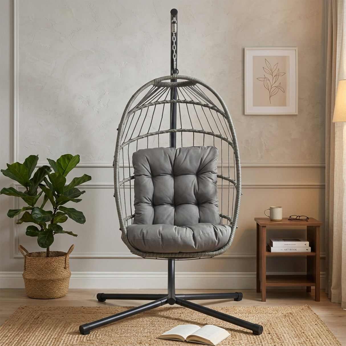 Poltrona sospesa a uovo in rattan grigio con cuscino imbottito, struttura nera, ambiente moderno e accogliente con piante e decorazioni