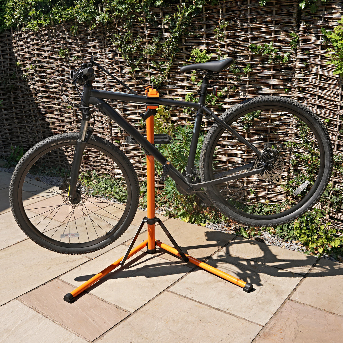 Cavalletto riparazione bici nero e arancione, robusto, con struttura pieghevole e supporto per bici in posizione verticale su pavimento in pietra