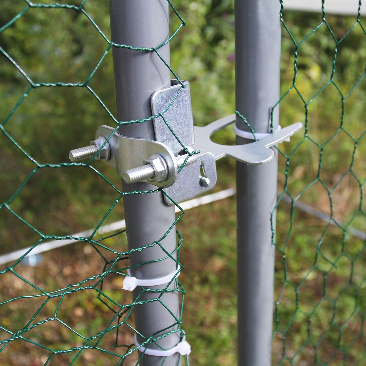 Dettaglio della chiusura metallica su un palo grigio, con rete verde per recinzione pollaio, ideale per allevamento all'aperto