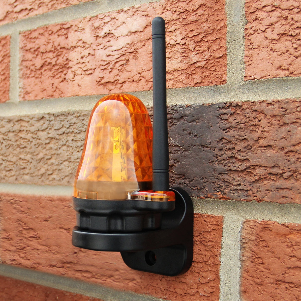 Lampada di segnalazione arancione con antenna, montata su muro di mattoni, design moderno e texture a rombi per visibilità elevata