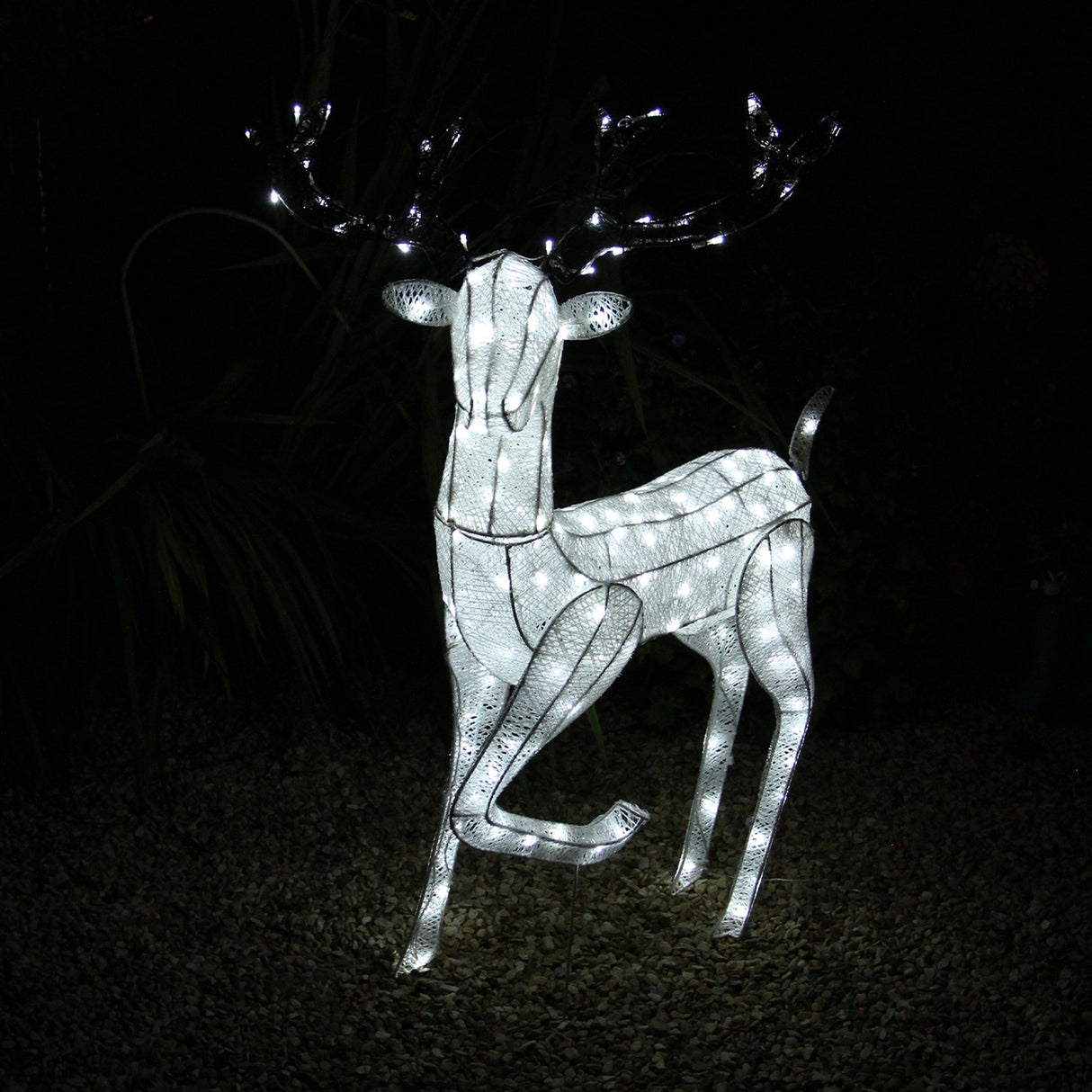 Renna di Natale luminosa maschio, bianca, con luci LED, posizionata su uno sfondo scuro, con corna decorate e dettagli eleganti