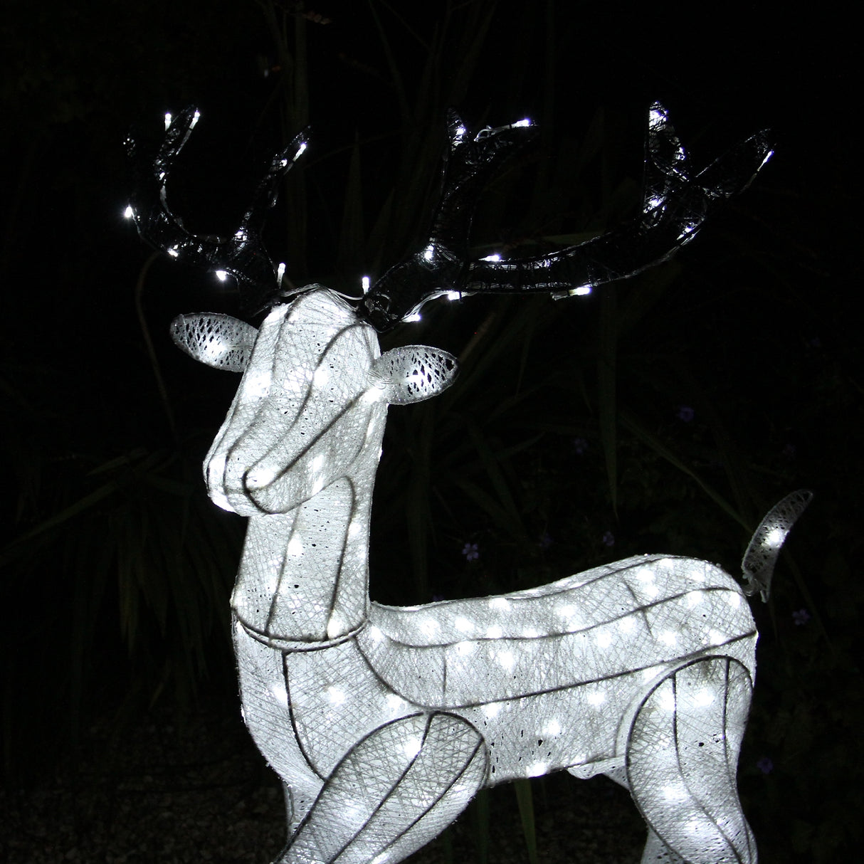 Renna di Natale luminosa maschile in bianco, con dettagli in rete e luci LED che brillano, posizionata su sfondo scuro