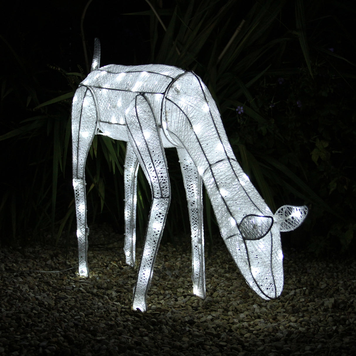 Renna di Natale luminosa femmina, realizzata in metallo bianco con luci LED, posizionata su un fondo di ciottoli e piante verdi