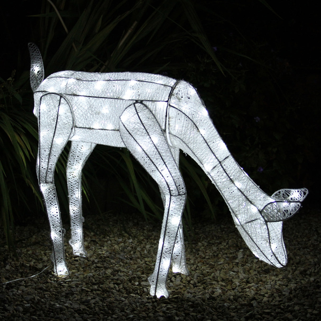 Renna di Natale luminosa femmina, realizzata in metallo bianco con luci LED, che si abbassa per mangiare, su sfondo di ghiaia