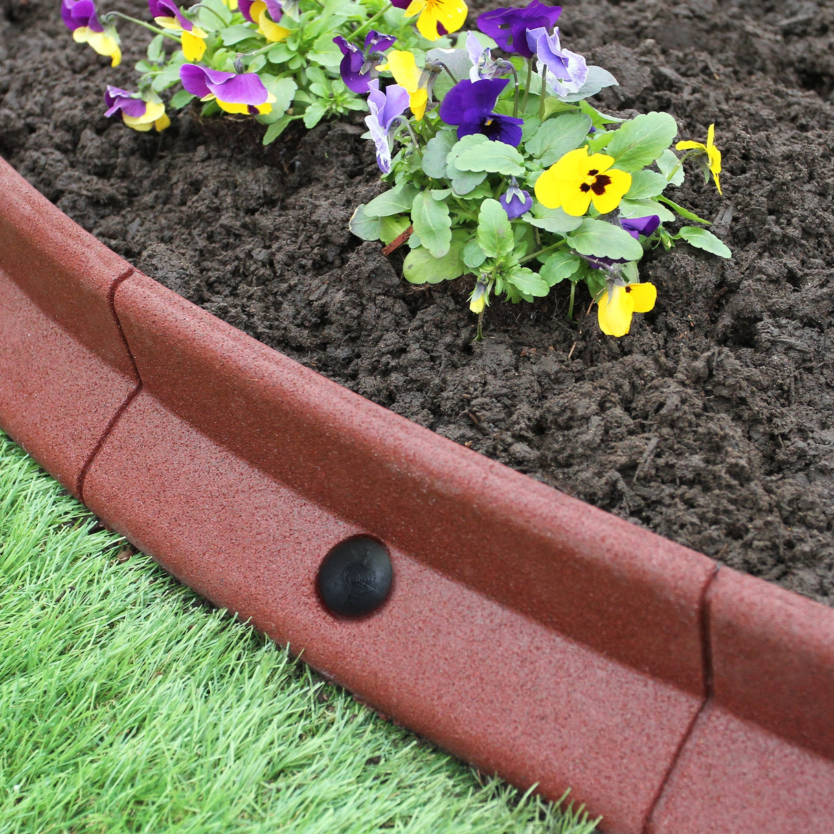 Bordatura da giardino flessibile in terracotta, con fiori viola e gialli, su terreno scuro e prato verde, per delimitare aiuole