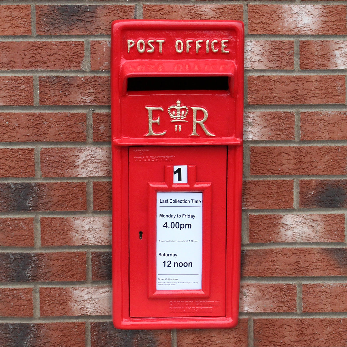 Cassetta postale britannica rossa con dettagli dorati, montata su un muro di mattoni, con orari di raccolta visibili