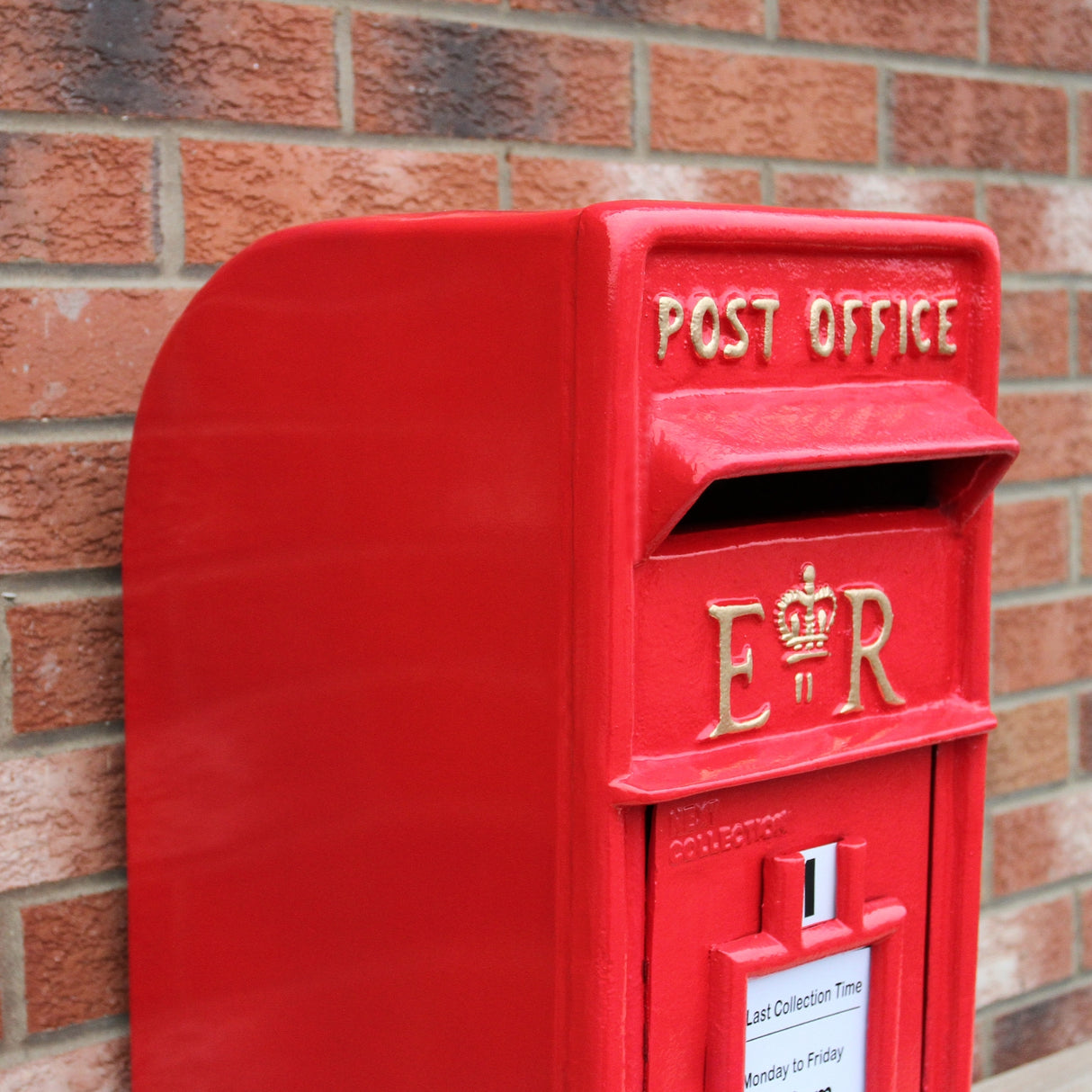 Cassetta postale britannica rossa con dettagli dorati, forma rettangolare e superficie liscia, posizionata su un muro di mattoni