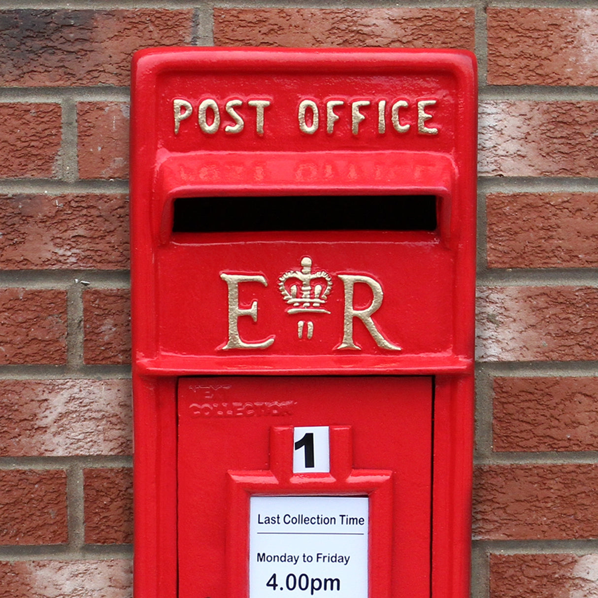 Cassetta postale britannica rossa con dettagli dorati, piedistallo, e avviso di raccolta, su sfondo di mattoni
