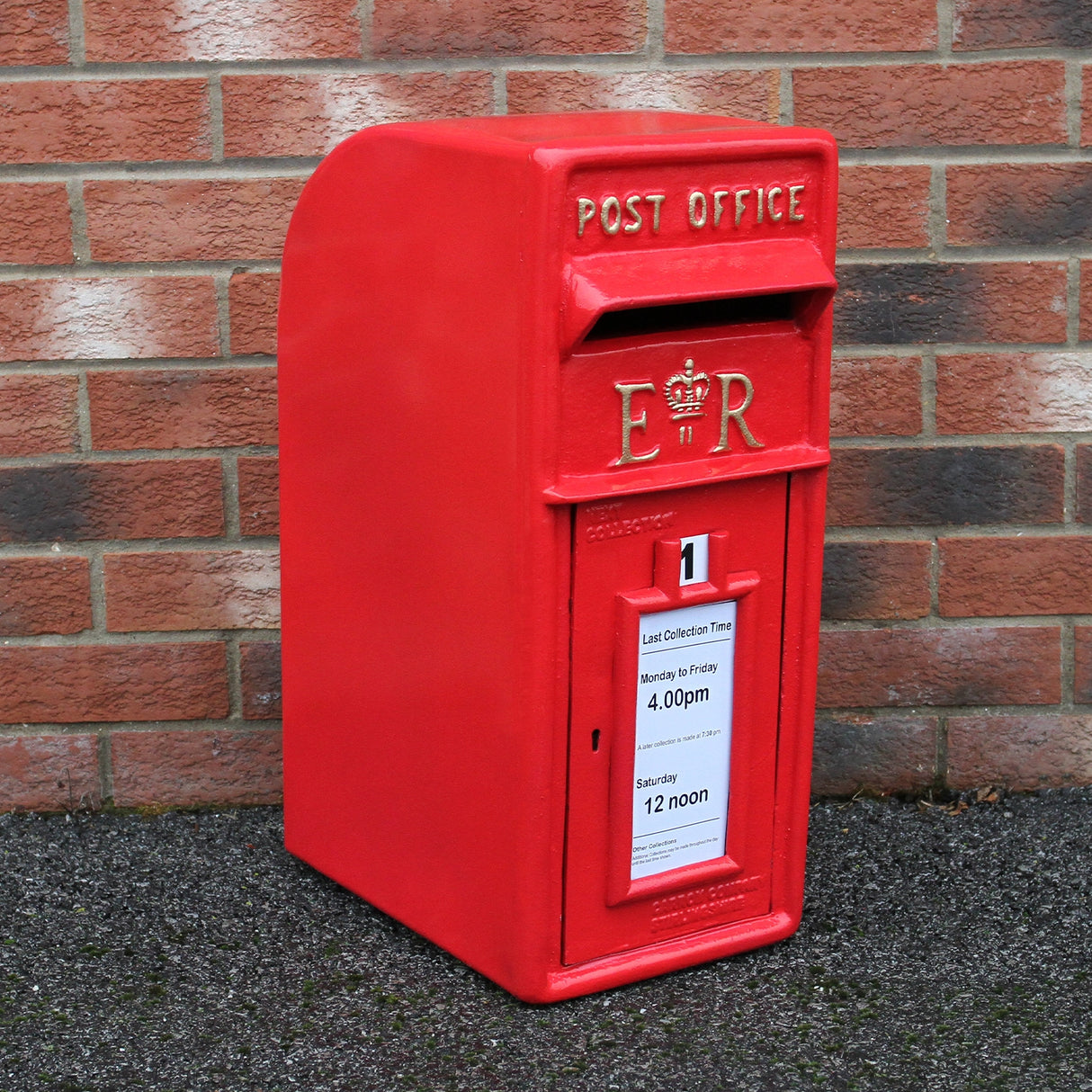Cassetta postale britannica rossa con piedistallo, decorata con il simbolo ER e un avviso di raccolta, su sfondo di mattoni