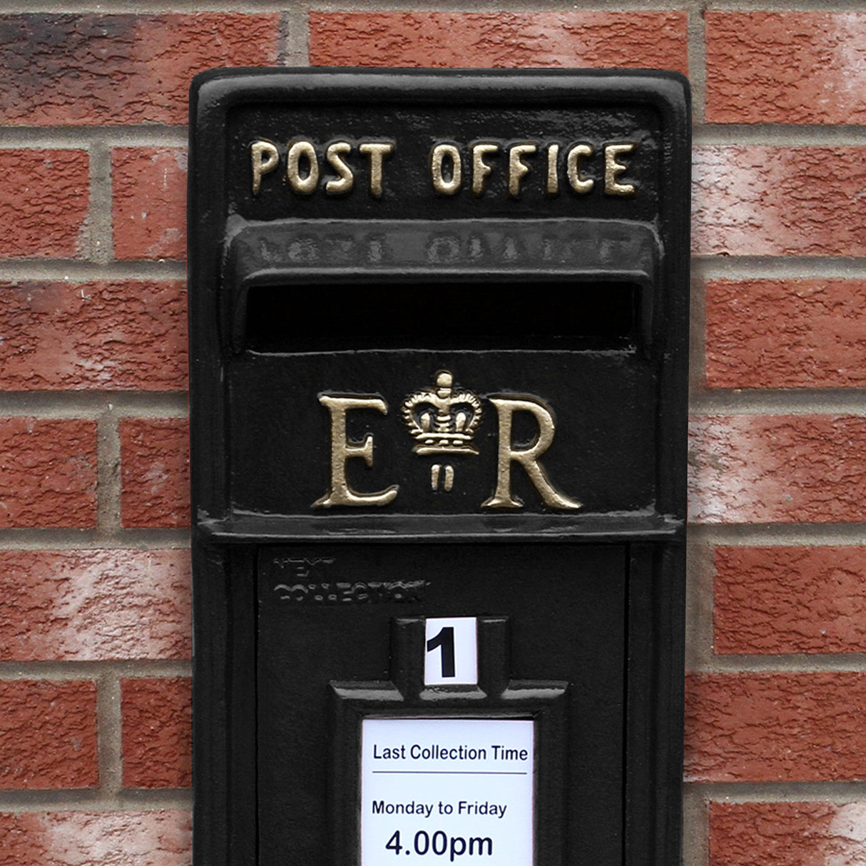 Cassetta postale britannica nera con piedistallo, decorata con dettagli dorati e simbolo reale, su sfondo di mattoni rossi