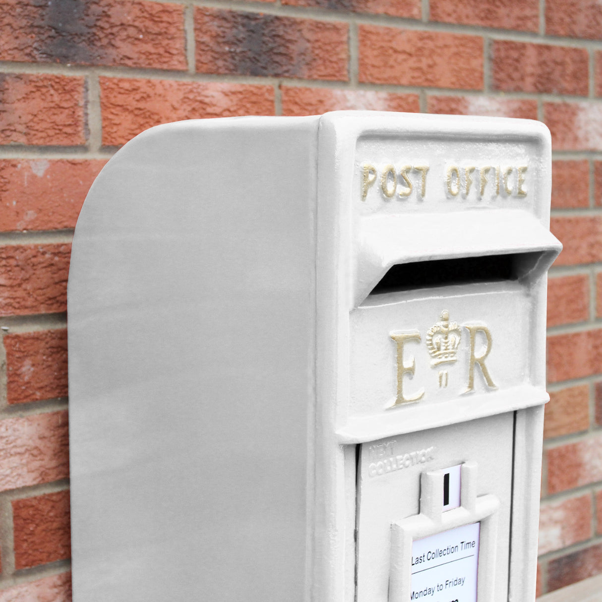 Cassetta postale britannica bianca con dettagli dorati, forma rettangolare e texture liscia, posizionata su muro di mattoni rossi