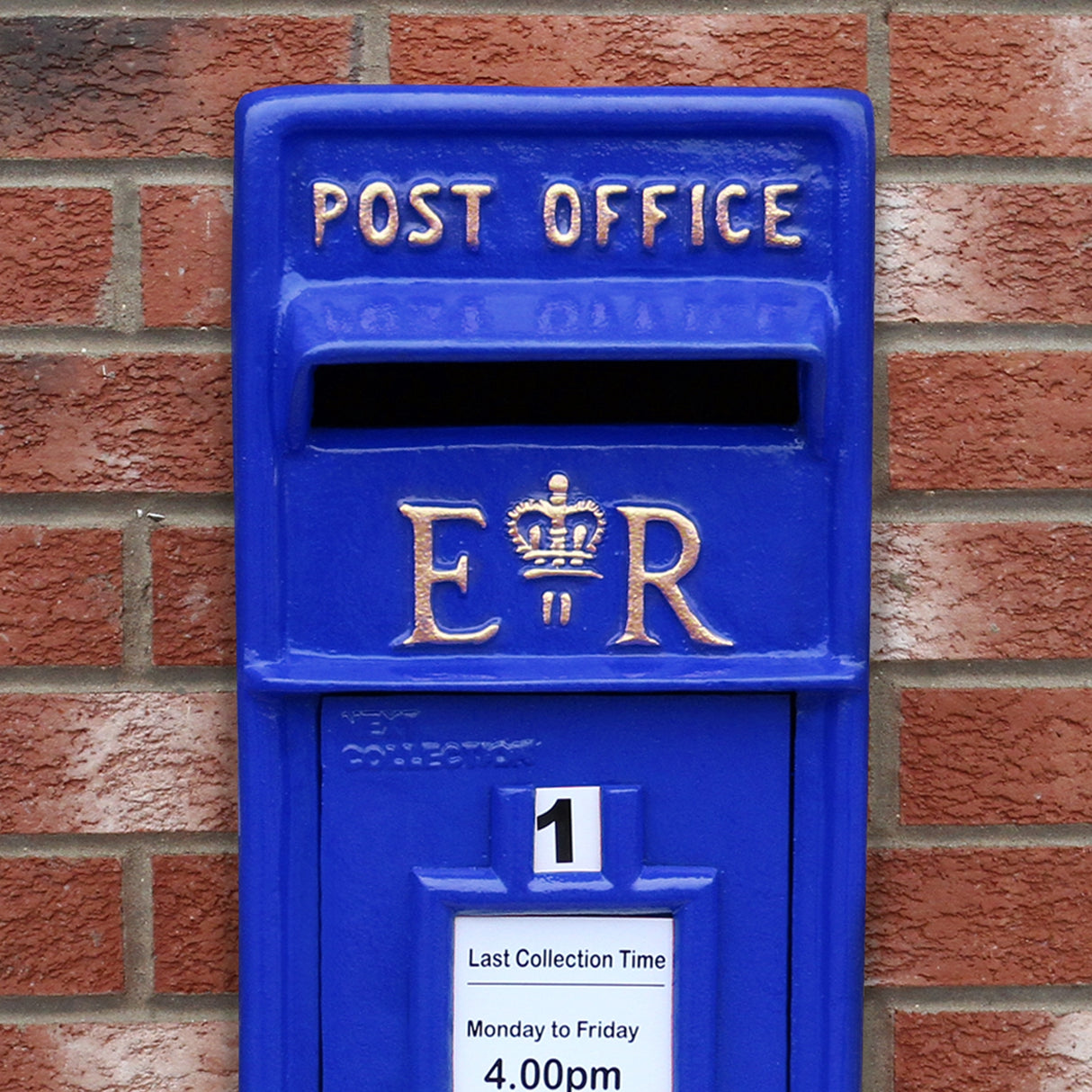 Cassetta postale britannica blu con dettagli dorati, logo E.R. e fessura per la posta, su sfondo di mattoni rossi