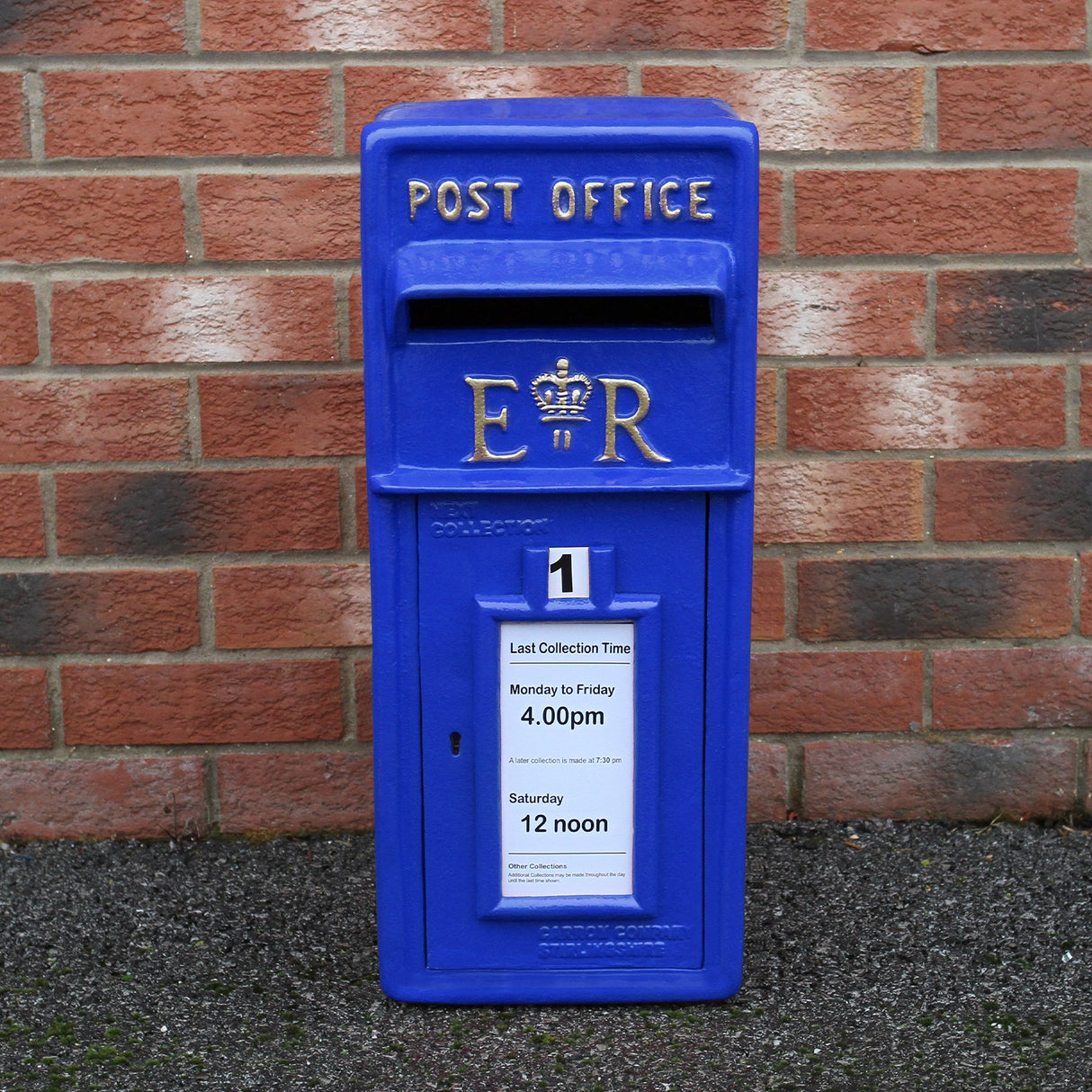 Cassetta postale britannica blu con dettagli dorati, etichetta di raccolta e sfondo di mattoni rossi, stile vintage