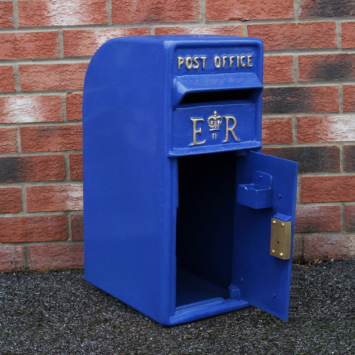 Cassetta postale britannica blu con finitura lucida, decorata con lettere dorate "ER" e sportello aperto su sfondo di mattoni rossi