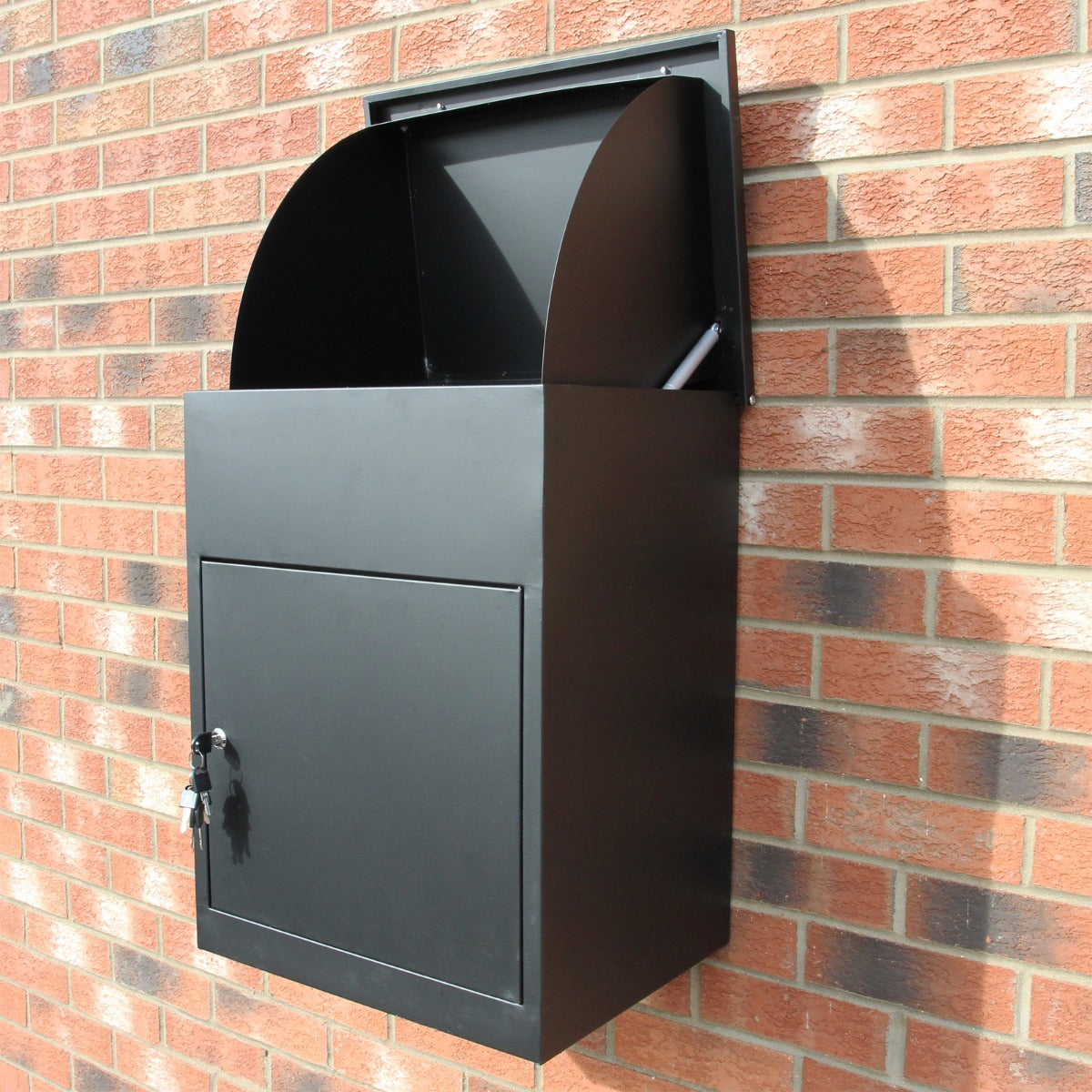 Cassetta postale per pacchi nera, in metallo, con design moderno e chiusura a chiave, montata su muro di mattoni rossi