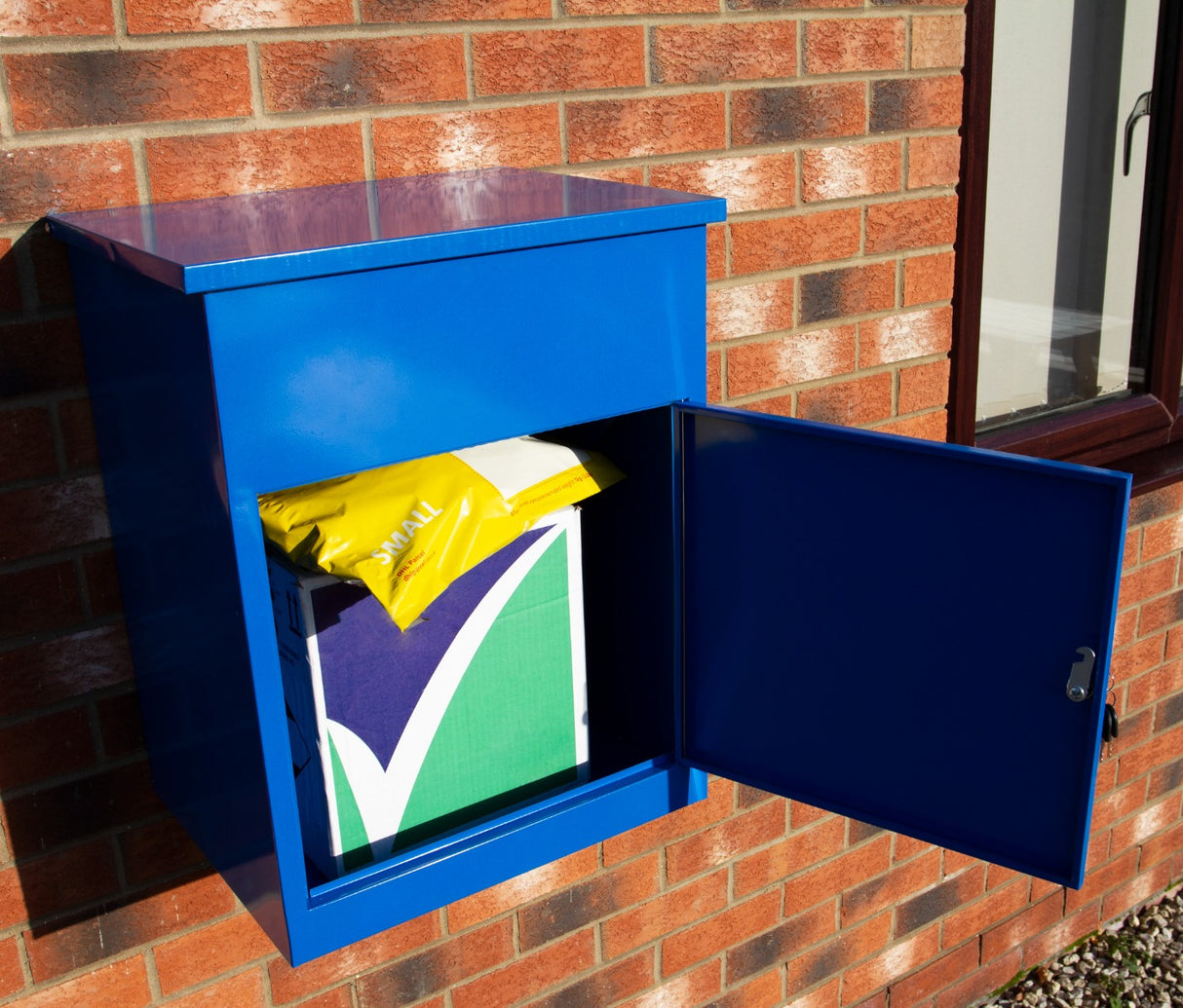 Cassetta postale per pacchi di colore blu brillante, con porta aperta che mostra un pacco giallo e verde all'interno, su sfondo di mattoni rossi
