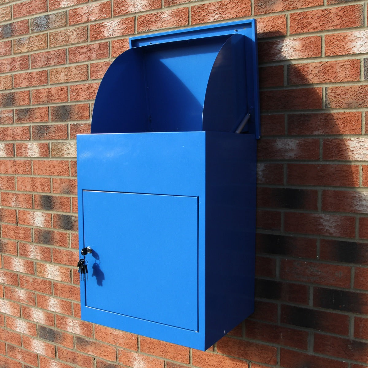 Cassetta postale per pacchi di colore blu brillante, con apertura superiore e serratura, montata su muro di mattoni rossi