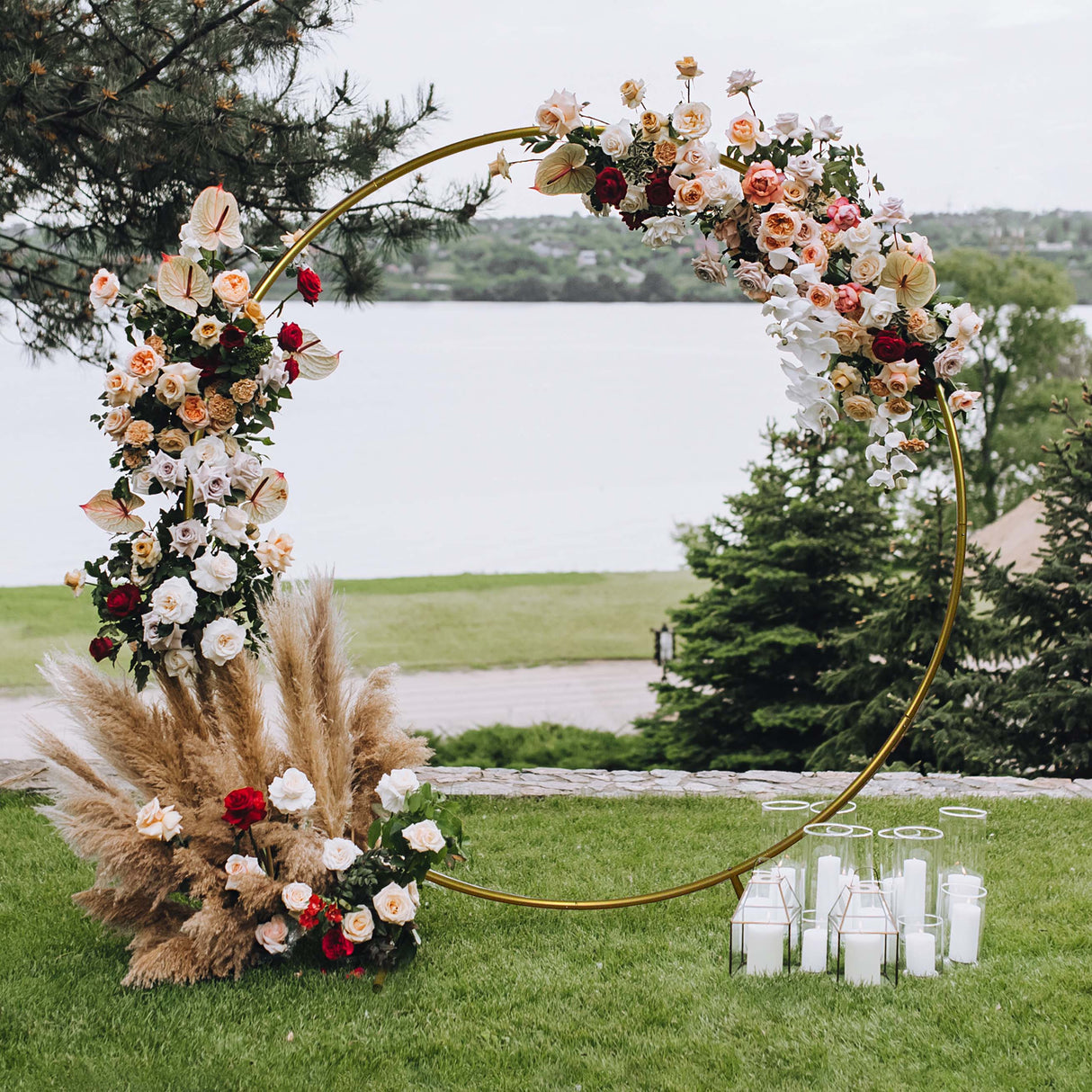 Arco decorativo dorato per matrimoni, adornato con fiori colorati e piante, circondato da candele e vegetazione verdeggiante
