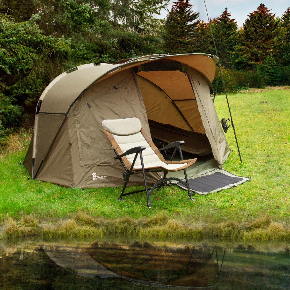 Tenda bivvy da pesca per 2 persone, color sabbia, con sedia pieghevole accanto, situata su prato verde vicino a uno stagno